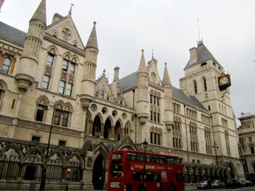 A double-decker bus pulls up in front of a large, gothic-style building.