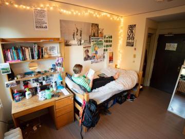 young woman sitting across a bed in dorm room