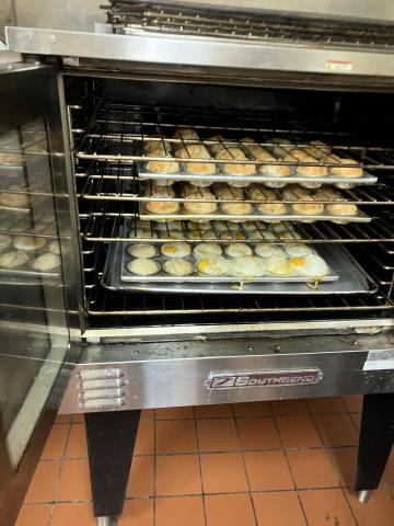 Picture of the inside of an oven. There are four racks. On the upper three racks there are rolls baking in muffin tins. On the lowest rack there are cooked sunny side up eggs baking in muffin tins.