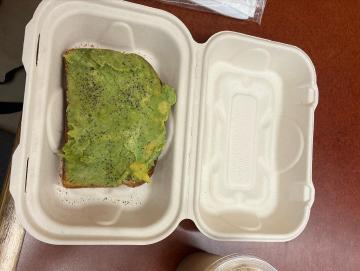 A cardboard box containing a scrumptious looking slice of everything avocado toast.