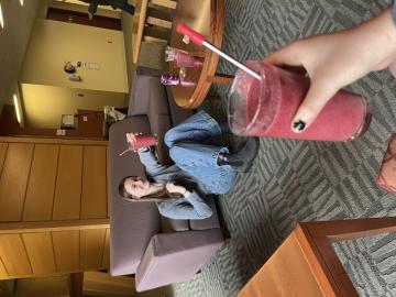 A smoothie in the foreground, a girl holding a smoothie behind it