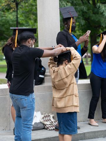 A male student helps another student put on a graduation cap.