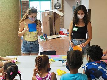 Two college students demonstrate paper folding for a group of children.
