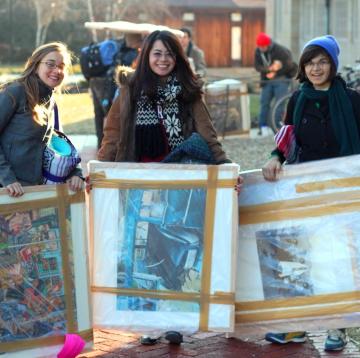 Three students stand with art they rented from the museum.