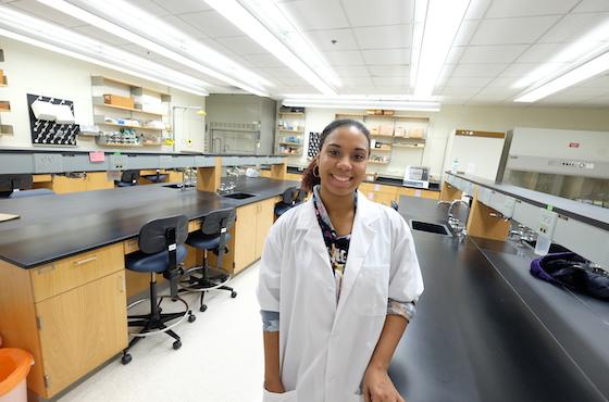 young black woman in white lab coat standing in a lab.