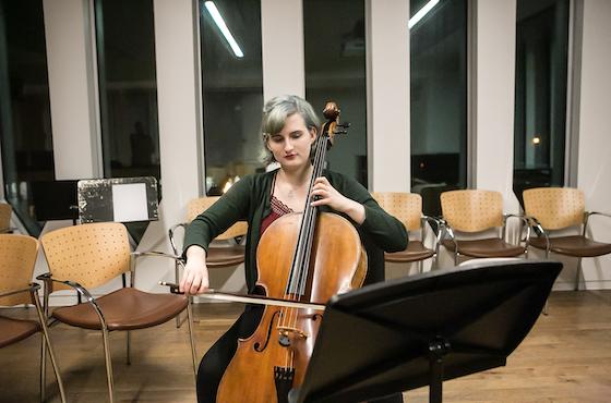 young woman practices her cello in a large practice room.