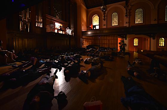 Under dim lighting in Finney Chapel, students lie on the stage beneath the pipe organ.