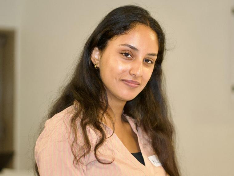 a person with long hair and a peach-colored shirt looks at the camera