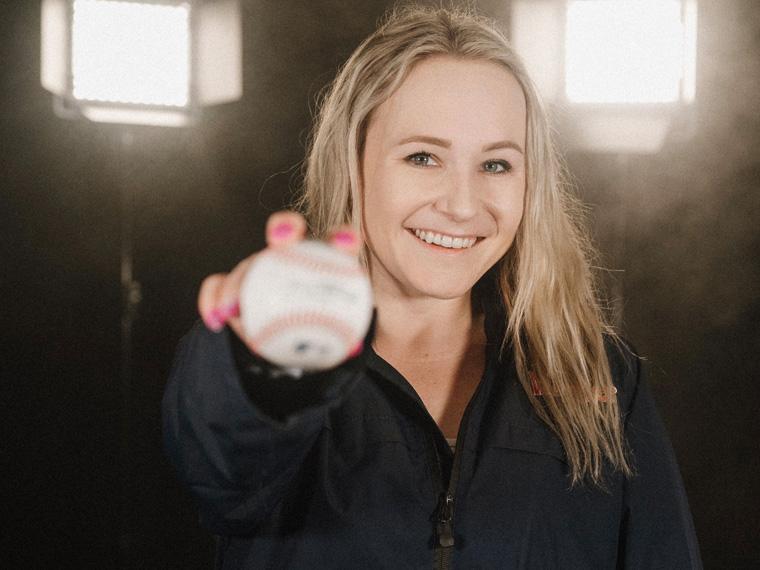 a person holds a baseball up to the camera as stadium lights behind them