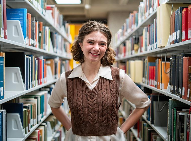 Student smiles while standing in bookstacks