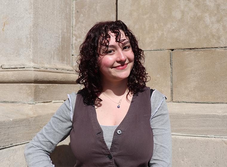 Student smiles while leaning against building