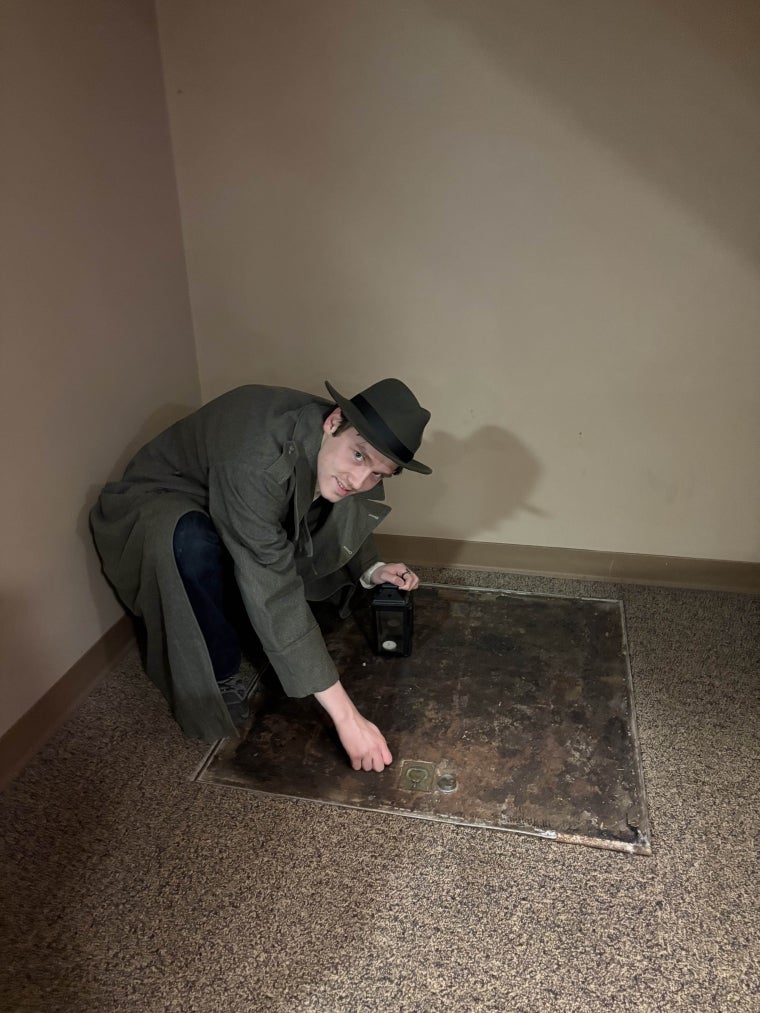 A figure in a coat crouches over an iron trapdoor.