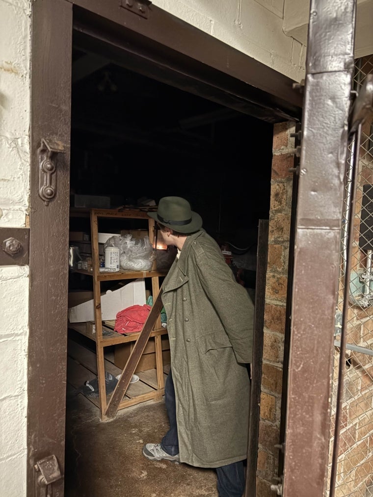 An open bulkhead door, with a figure in a coat holding a lantern to illuminate the dark room beyond.