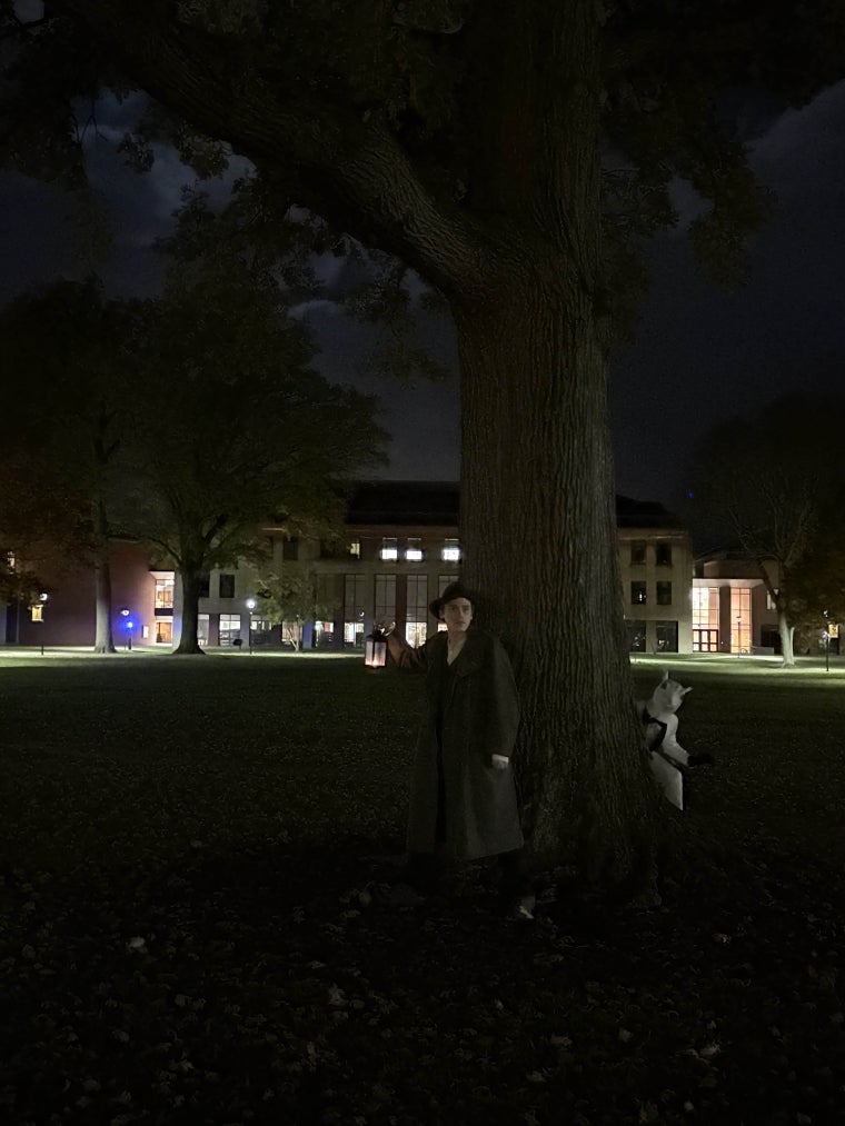 A figure in a coat stands on North Quad in Oberlin, while a white squirrel in a white tuxedo lurks behind a tree.