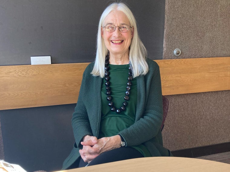 a person with long white hair wearing dark green clothes smiles for the camera