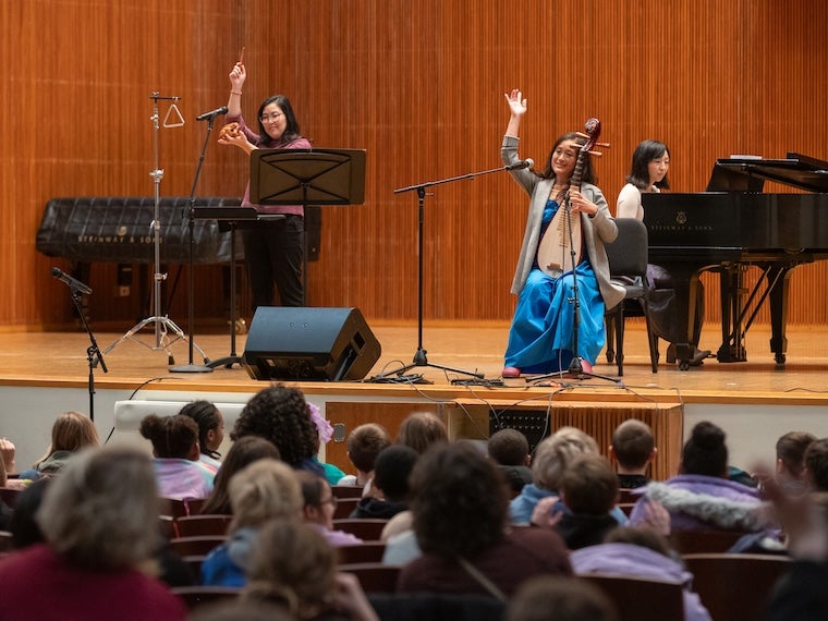 Musicians perform on stage in front of a seated audience in a concert hall.