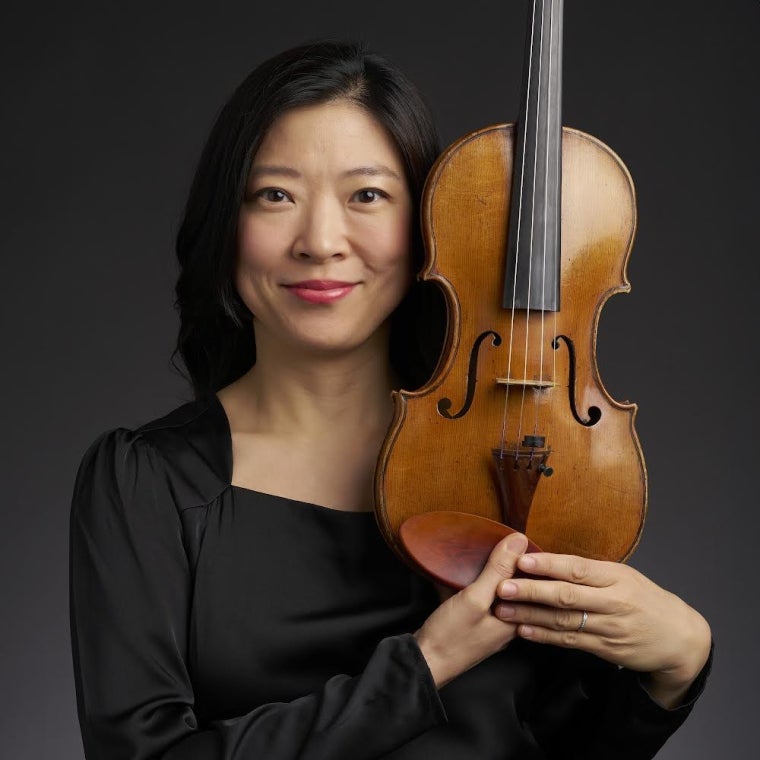 a smiling person holds a violin next to her face