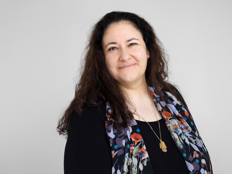 a person with long dark hair wearing a colorful vest smiles