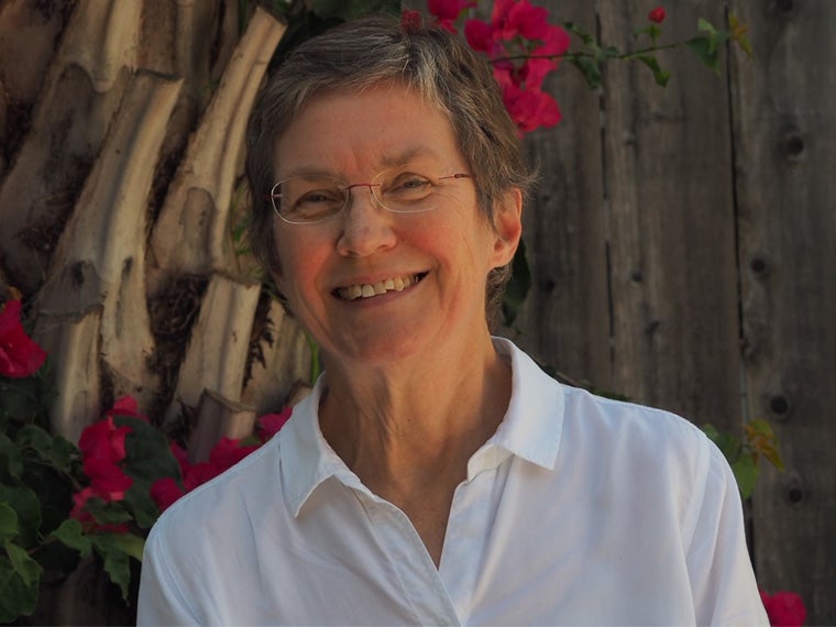 a person wearing a white collared shirt and glasses stands in front of magenta flowers