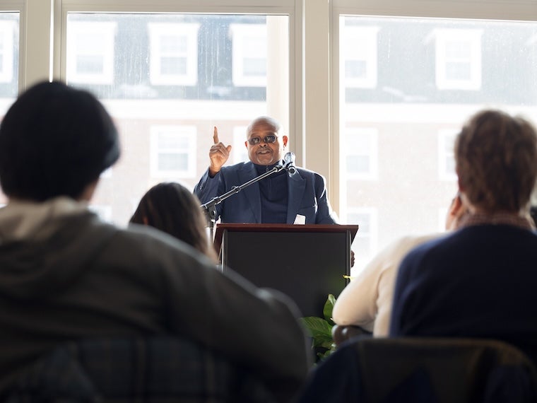 A.G. Miller speaking at a podium to an audience indoors.