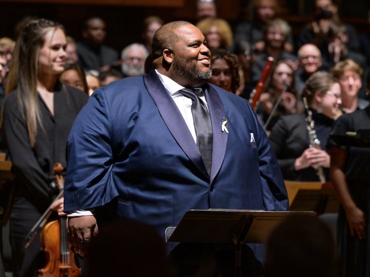 Limmie Pulliam at a podium, cheerfully looking at the audience with an orchestra behind him.