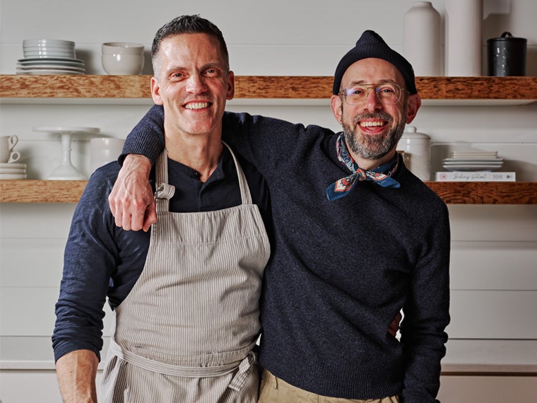 two smiling people stand next to each other in a kitchen