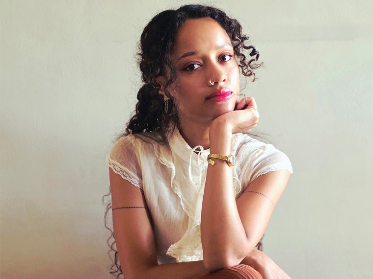 a person with dark curly hair wearing a white shirt leaning their head in their left hand