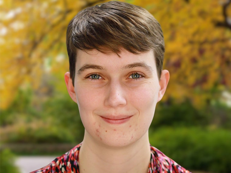 a person with short brown hair smiling in front of yellow fall foliage