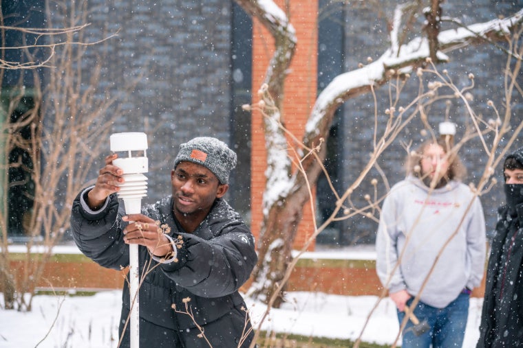 a person wearing winter gear focuses on a science experiment outside in snowy weather