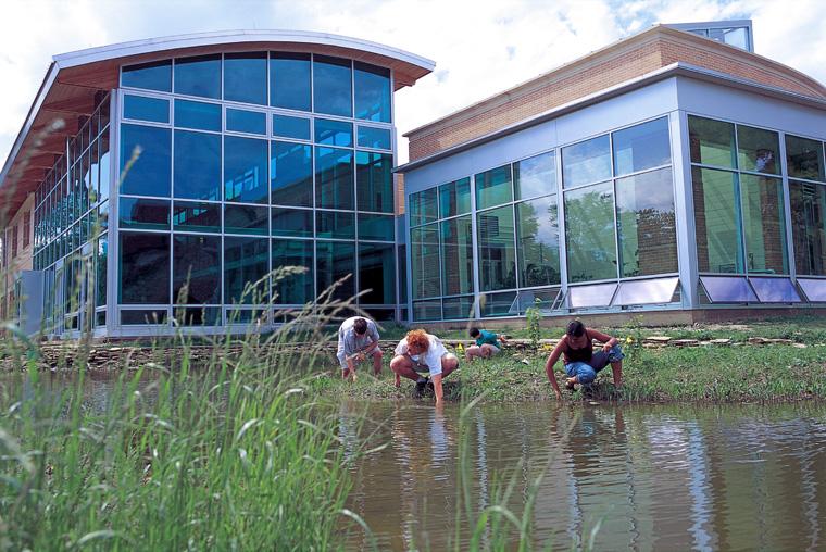 Students crouch at the edge of the pond behind  the Adam Joseph Lewis Center.