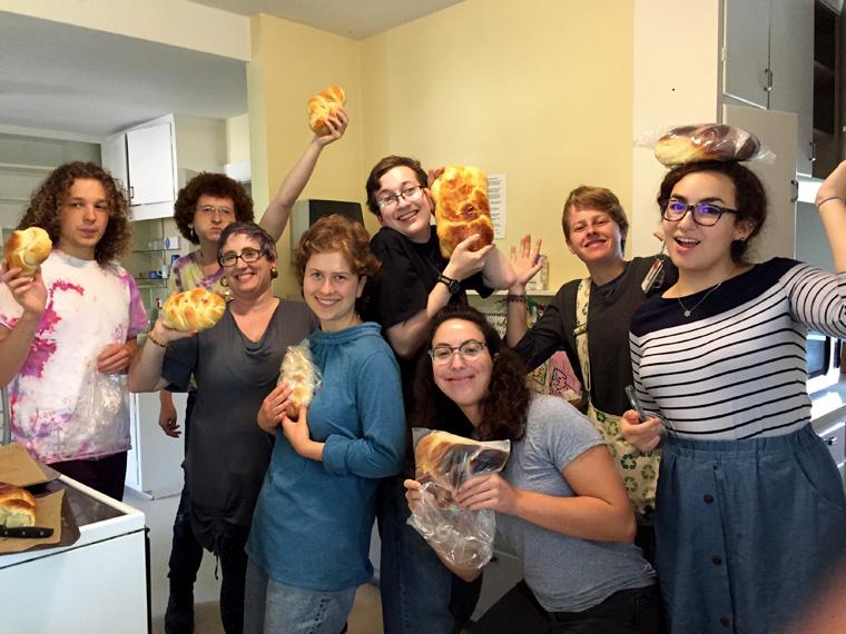 Happy students in a kitchen show off the loaves of challah they've just baked.