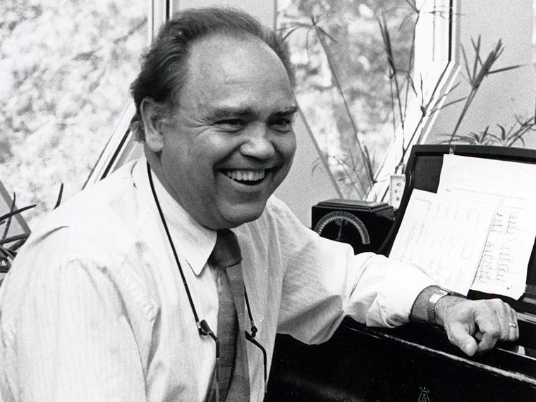 Black and white photo of Richard Miller seated at a piano, smiling