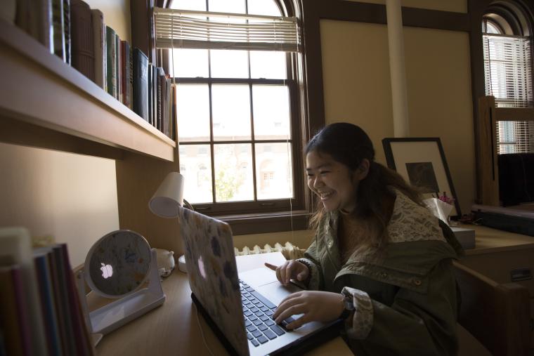 A female student smiling and looking at her laptop.