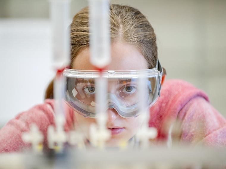 female student with science goggles looking straight at test tubes.