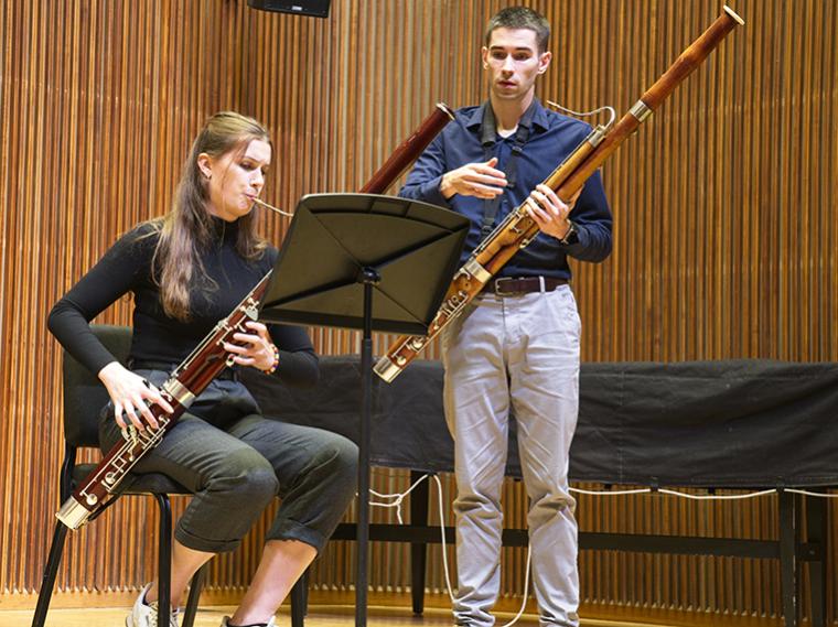 seated bassoon player is coached by standing bassoon teacher on stage of small recital hall