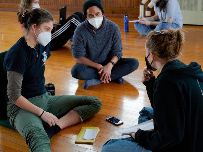 Students sit in small groups on the floor of the dance studio.