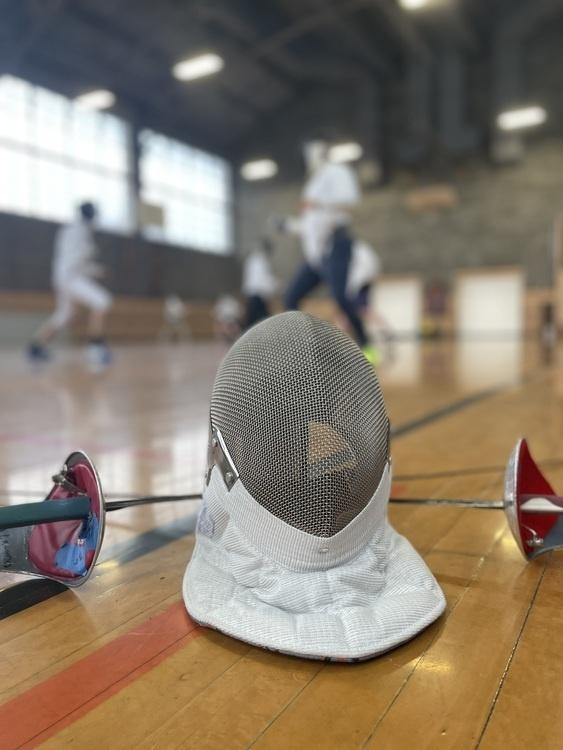 Sabre mask and swords on the floor with fencers in the background