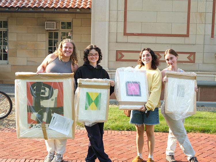 Four light-skinned students stand together displaying their Art Rental selections.