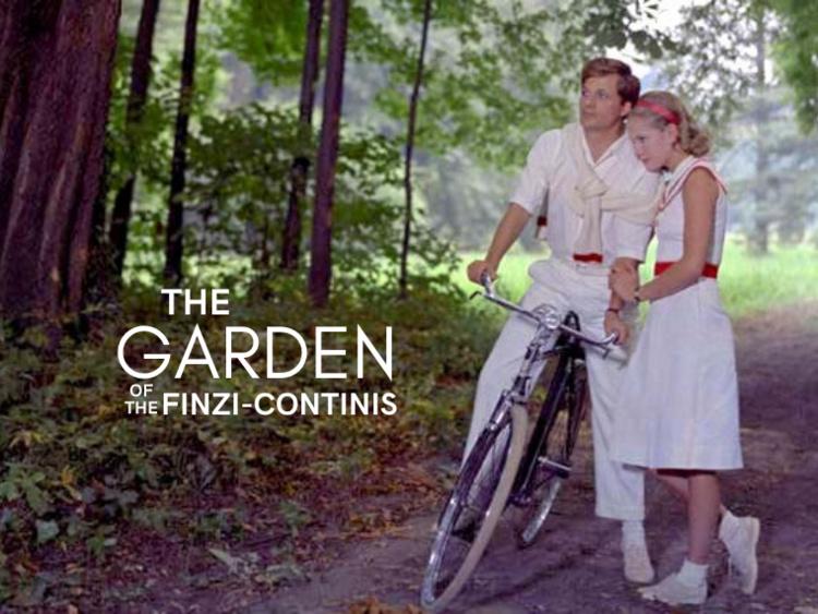 A person on a bike with another standing next to them in a garden
