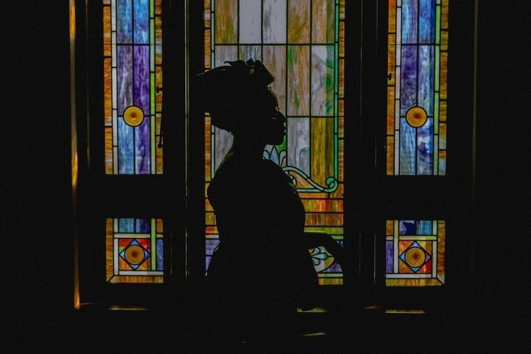silhouette of a woman lit from behind through stained glass windows