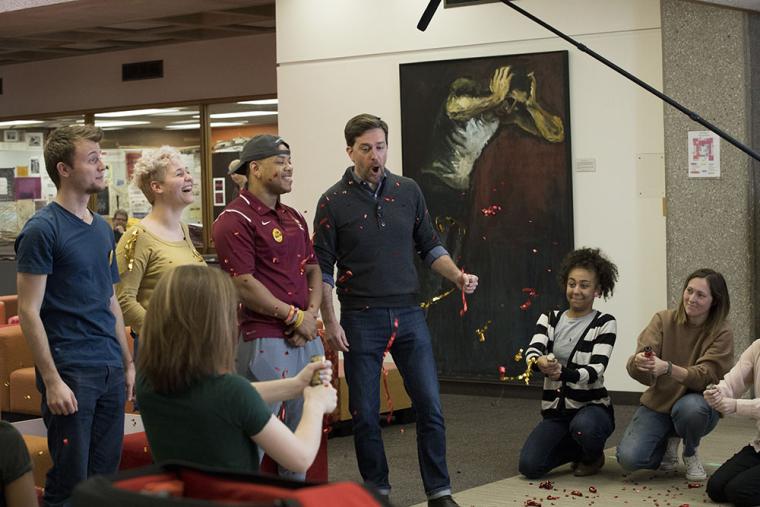 A video crew tosses confetti while alumnus Ed Helms is on camera with students.