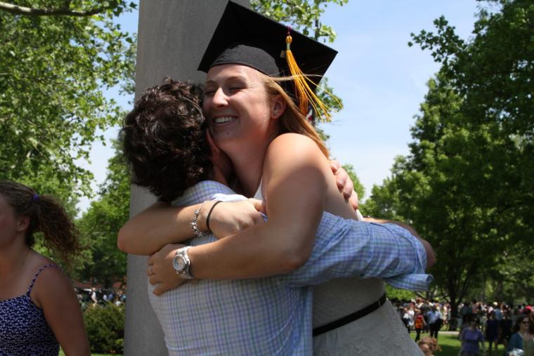 A woman wearing a commencement cap embraces another person outdoors