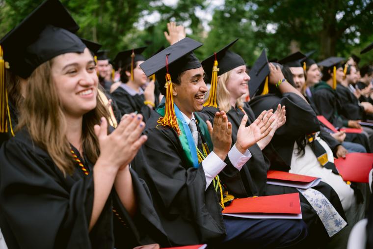 Seated students applaud during commencement addresses.