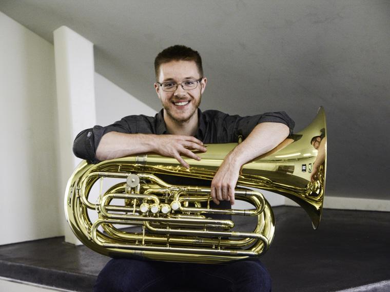 male student sitting with a tuba and smiling.
