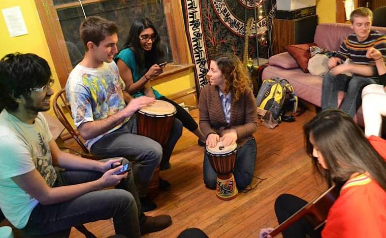 Group of people seated in a circle playing music with an acoustic guitar and djembe drums.