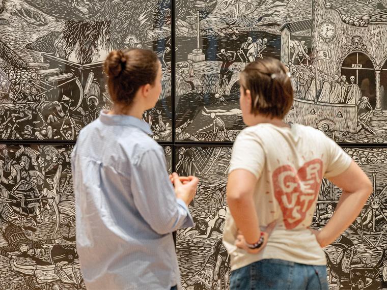 two people look at a large piece of art on the wall