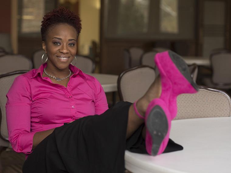 Armina Patton sits wearing a pink shirt and black pants, with her feet up