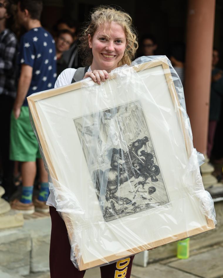 Student holds a framed drawing, which is wrapped in plastic.