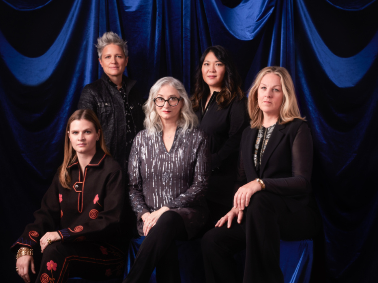 five women some standing some sitting with blue curtain backdrop