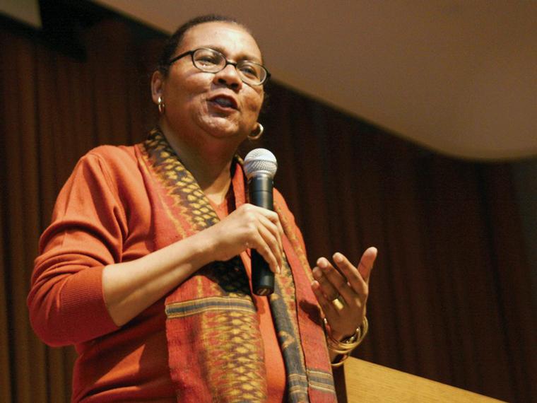 Bell Hooks wearing orange top and talking on stage with a microphone in hand